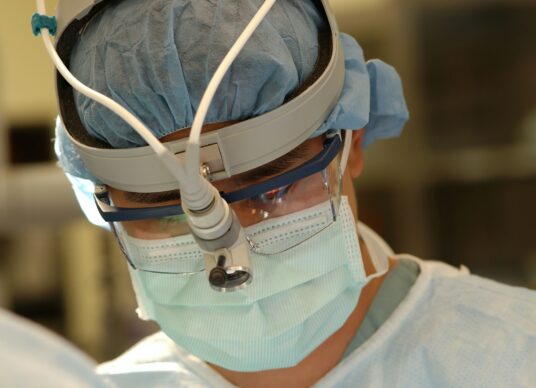 Healthcare provider in mask and head-mounted microscope